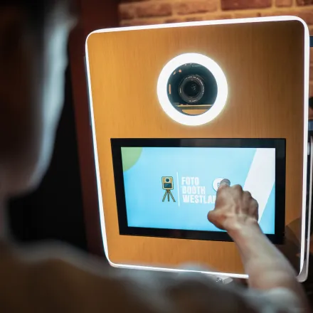 Een gast tikt op het touchscreen van de fotobooth; de ring rond de lens licht op